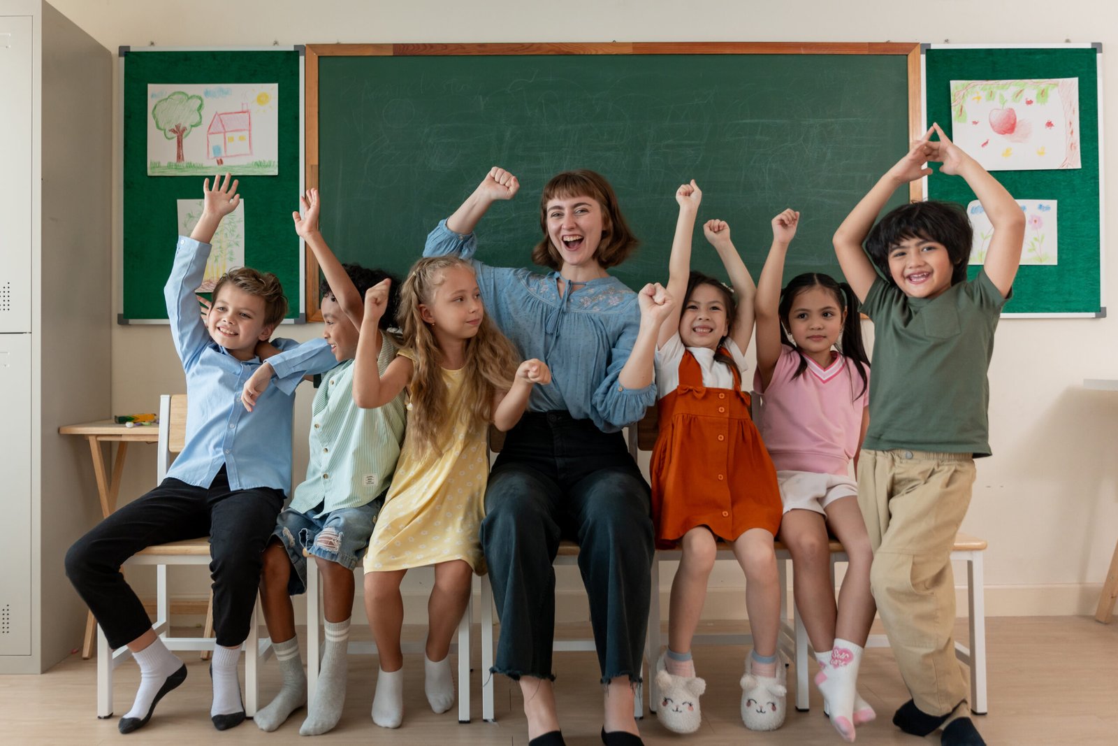 Portrait of diversity student sitting on chair with teacher at school. Group of schoolboy and girl enjoy back to school in classroom then looking at camera with instructor at elementary kindergarten.